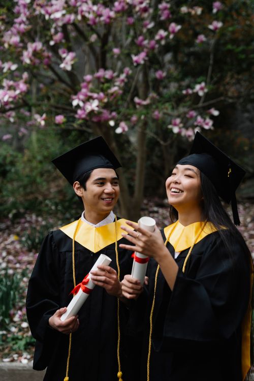 Two graduates in academic gowns smiling and holding their diplomas